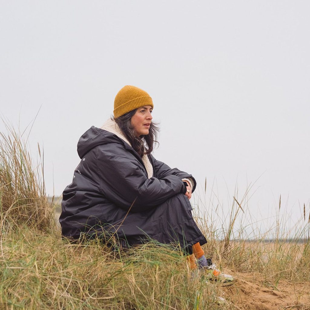 Sarah sitting in the sand dunes looking out to sea in Winter